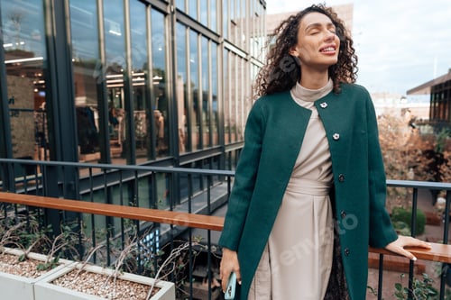 Preview: Portrait of young woman in green coat with curly hair in the city