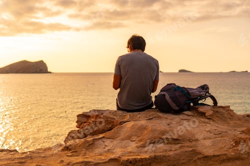Preview: A tourist sitting watching the sunset at Cala Comte beach on the island of Ibiza. Balearic