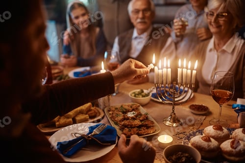Preview: Close up of man lighting the menorah during family meal on Hanukkah.
