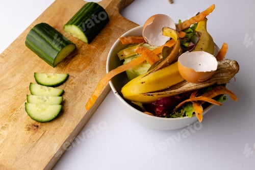 Preview: Cucumber on chopping board with organic food waste in kitchen composting bin