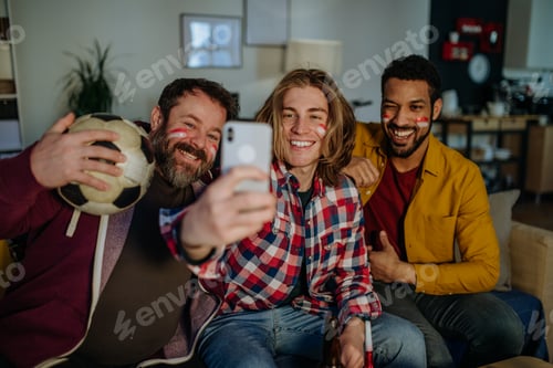 Preview: Happy football fans friends watching football at home and taking selfie