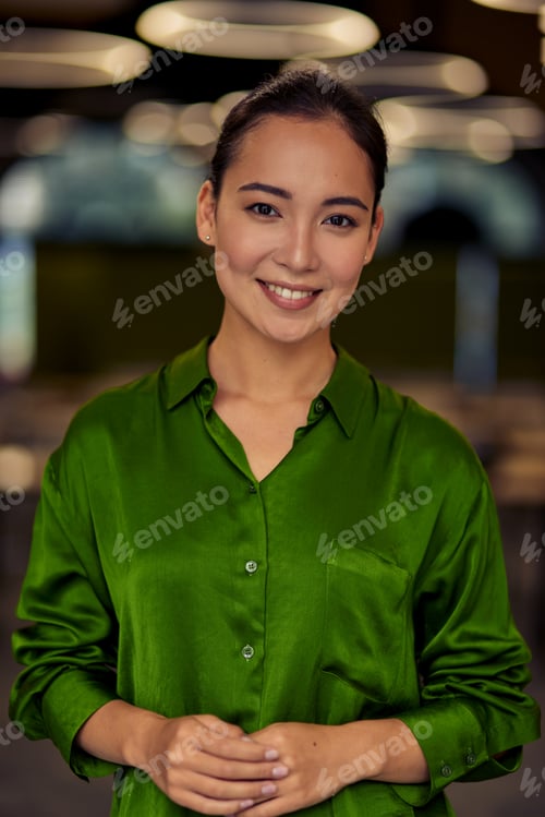 Preview: Vertical shot of a young happy asian business woman in green silk shirt looking at camera and