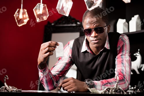 Preview: Young african man in stylish casual clothing and sunglasses sitting at table and offering drugs in