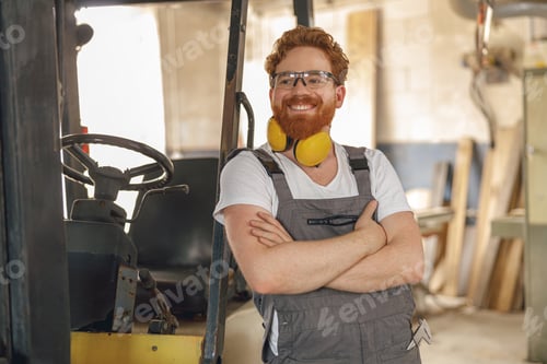 Preview: Portrait of smiling carpenter in eyeglasses standing on the background on carpentry workshop