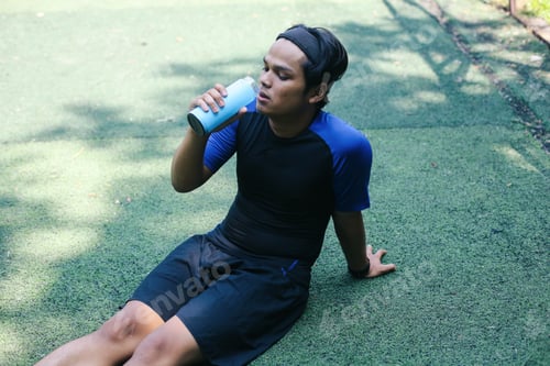 Preview: Sportsman Sitting On Grass Field Ground, Holding Bottle And Drinking water.