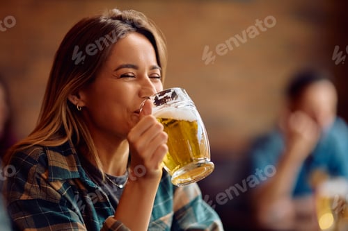 Preview: Happy woman drinking beer in a bar.