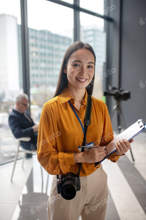 Preview: Dark-haired young cute reporter with camera feeling happy