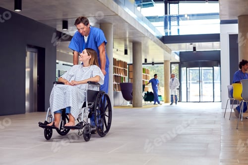 Preview: Male Nurse Wearing Scrubs Pushing Female Patient In Wheelchair Through Hospital Building