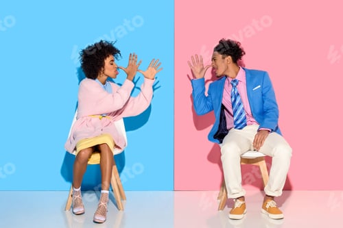 Preview: african american couple grimace to each other while sitting on chairs against pink and blue wall