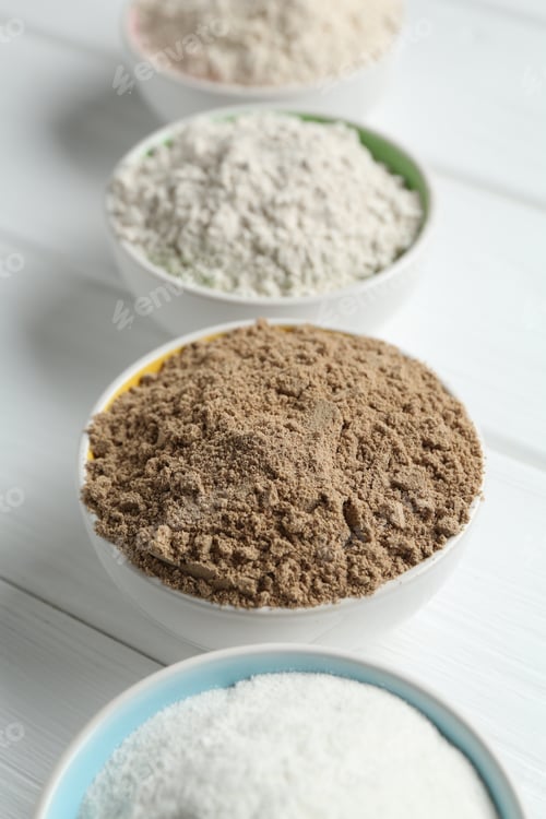 Preview: Different types of flour in bowls on white wooden table, closeup