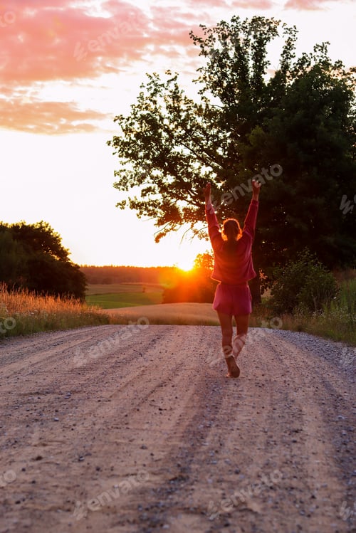 Preview: A happy woman is walking along a country road at sunset.
