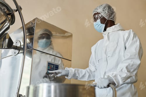 Preview: Black man wearing protective suit in factory workshop and pressing buttons