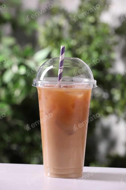 Preview: Tasty iced coffee on white table against blurred background