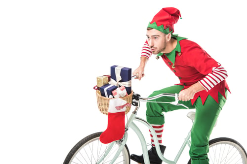 Preview: focused man in christmas elf costume riding bike and transporting presents in basket isolated on