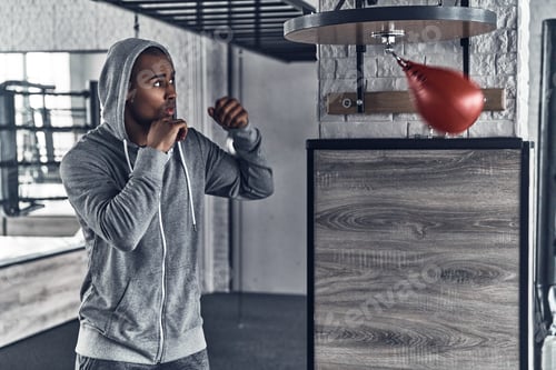 Preview: Nothing but success. Handsome young African man in sport clothing boxing while exercising in the gym