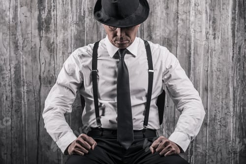 Preview: Hidden threat. Bossy senior man in gangster clothing sitting at the chair and against a wall
