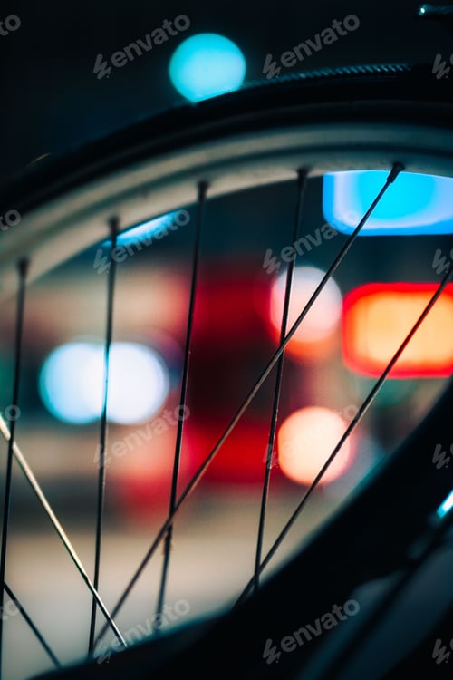Preview: Close-up of a bicycle wheel with bright lights illuminating the blurry background