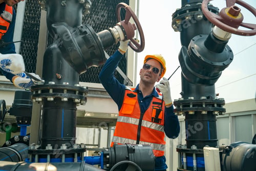Preview: Industrial worker in hard hat and safety vest operating a large valve with a radio