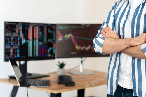 Preview: Cropped view of crypto trader holding arms crossed in modern office, monitors with crypto chart