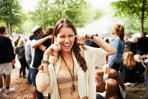 Preview: I cant hear you. A young woman struggling to hear on her smartphone at an outdoors festival.