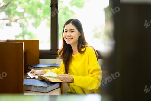 Preview: Cheerful young asian female student doing class assignment, reading book in library.