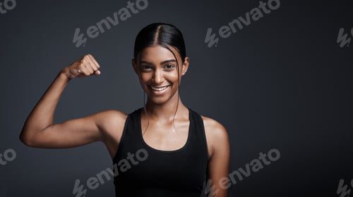 Preview: Studio portrait of a young sportswoman flexing her bicep against a gray background
