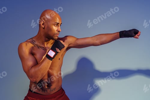 Preview: Professional kickboxer is training and practicing punch on studio background with shadows
