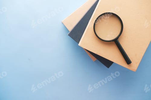 Preview: stack of book and magnifying glass on blue background .