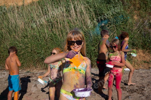 Preview: beautiful girl painted with colorful holi colors has fun on the beach in the company of her friends