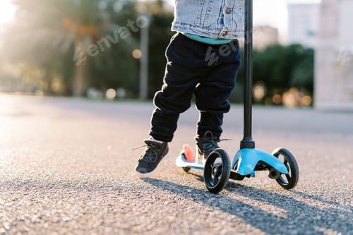 Preview: Small child rides a scooter along the road, pushing off with his foot. Cropped. Faceless