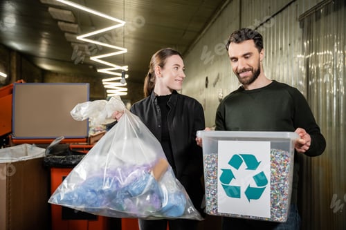 Preview: Smiling volunteer holding trash bag near man with bin and recycle sign in blurred waste disposal