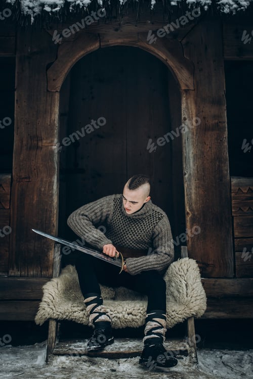 Preview: Portrait of strong viking warrior sharpening his sword, scandinavian viking cosplay