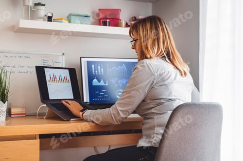 Preview: A woman working at a desk with two computer screens displaying data and graphs. She is focused on he