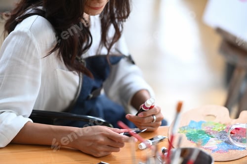 Preview: Cropped shot woman painter mixing color on palette at creative workplace.