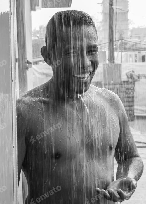 Preview: Black and white photo of an Asian man standing outside in a torrential downpour of rain to cool off.