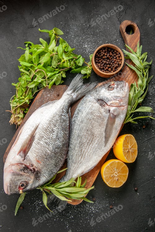 Preview: top view raw sea fish on chopping board onions black pepper in small bowl mint on black background