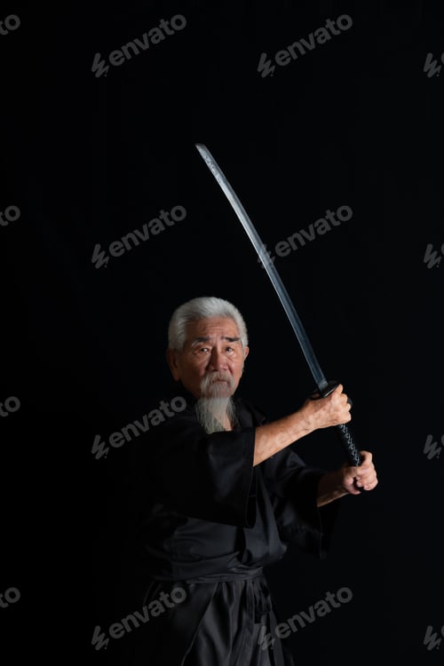 Preview: Senior Japanese samurai with katana sword on black background, studio shot