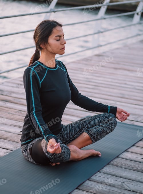 Preview: girl in black practicing in yoga meditation on wooden seafront. Woman in lotus pose