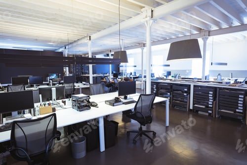 Preview: Empty swivel chairs with computers at desks in illuminated modern office