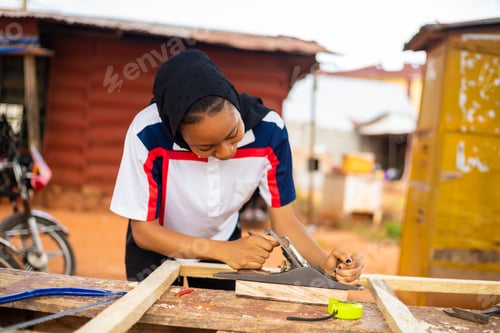 Preview: Selective focus shot of a young African female with a covered head making wooden frame