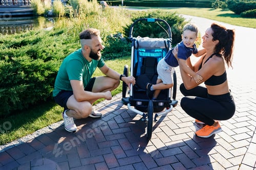 Vorschau: Glückliche sportliche Familie mit Kind in der Nähe des Joggingwagens nach dem Training im Stadtpark