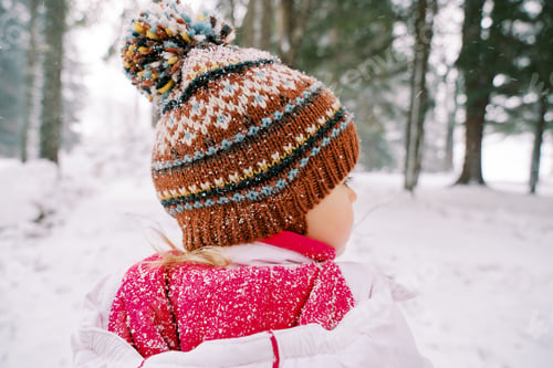 Preview: Little girl stands under snowfall in a snowy forest and looks to the side. Back view