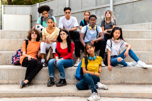 Preview: Multiracial teenage students sitting on steps looking at camera with serious expression.