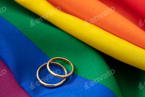 Preview: LGBT Gay marriage. Pair of golden rings on rainbow color textile, close up view. Copy space