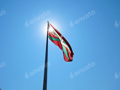 Preview: Ikurrina flag waving in the air against blue cloudless sky and covering the sun rays
