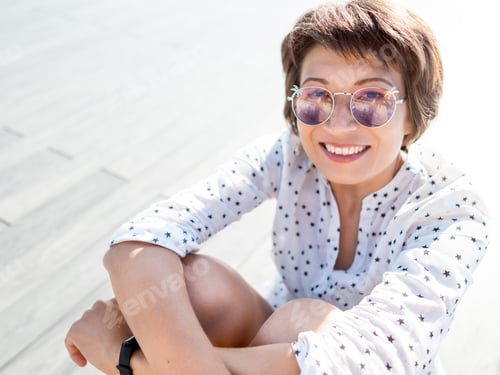Preview: Wind ruffles short hair of freckled woman with colorful sunglasses. Summer vibes.
