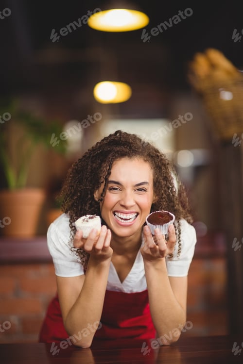 Preview: Portrait of a waitress showing two cupcakes at the coffee shop