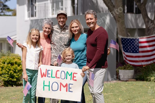 Preview: Happy caucasian soldier father, wife, children and parents outside home with welcome sign and flags