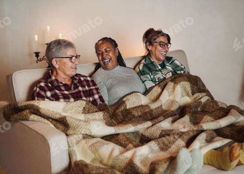 Preview: Elderly multiracial women having fun together sitting on the couch with blanket