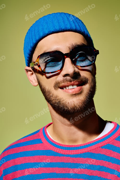 Preview: Young man showcases vibrant style in trendy sunglasses against a green backdrop